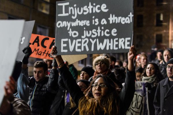 student holds sign at a rally saying injustice anywhere is a threat to justice everywhere