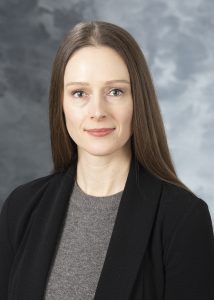 Jaimee Gilford, smiling white woman with straight brown hair, wearing a grey sweater and black blazer.