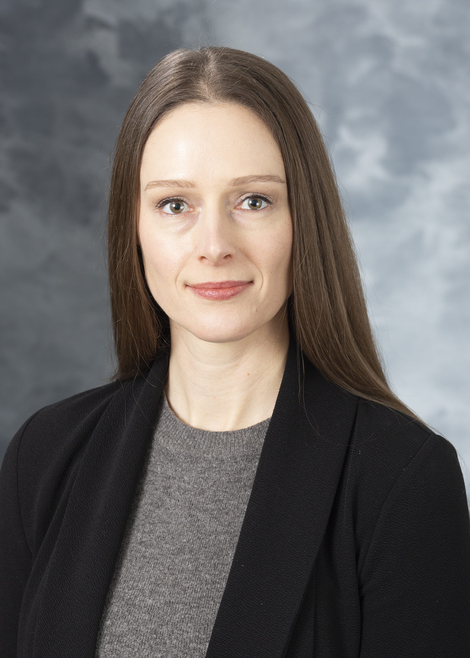 Jaimee Gilford, smiling white woman with straight brown hair, wearing a grey sweater and black blazer.