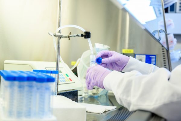 Purple gloved hands using lab equipment and small vials with blue lids.