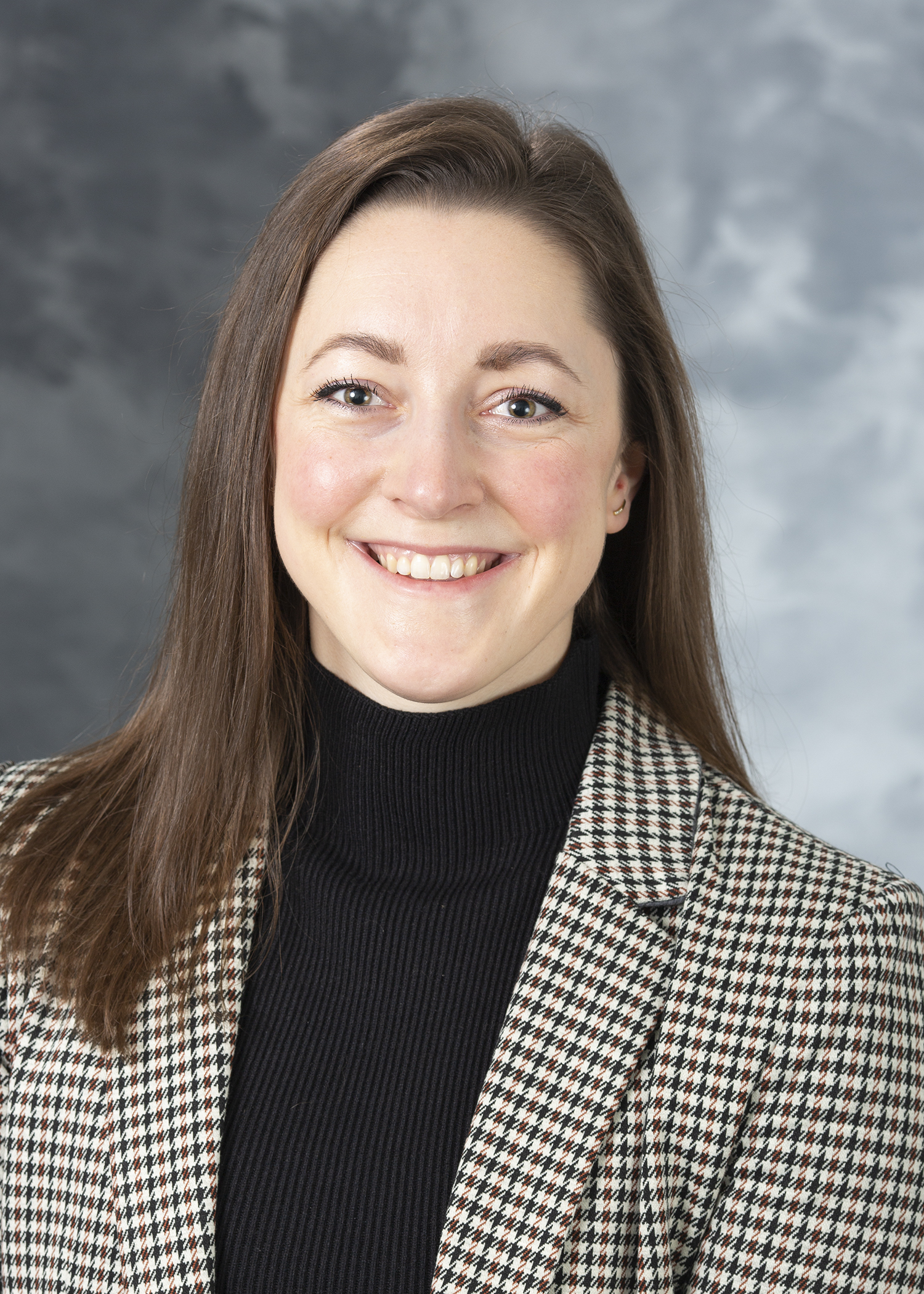 Taylor Buresch, Smiling woman with brown hair, wearing a black mockneck and houndstooth check patterned blazer.