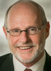 James Shepherd, Smiling man with light brown hair, a beard and glasses wearing a suit with a red tie.