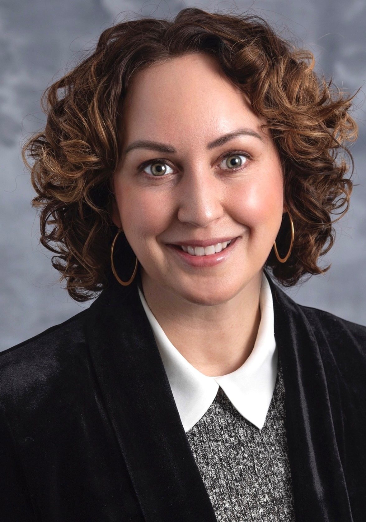 Jennifer Haese, smiling woman wearing a black blazer over a grey sweater with a white collar.
