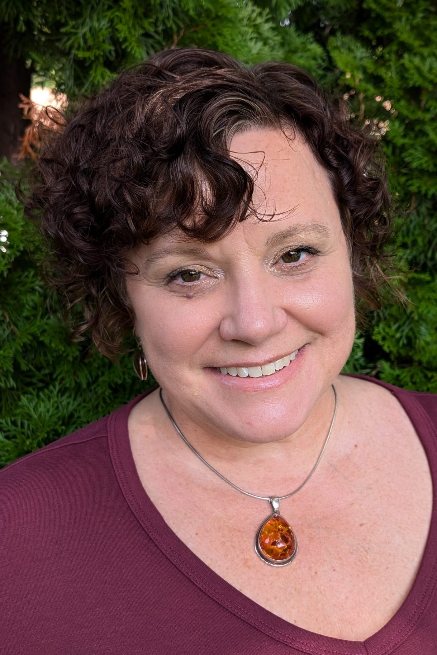 Julie Laundrie, a smiling woman with short, brown hair wearing a burgundy-colored shirt and a silver necklace with a large gemstone.