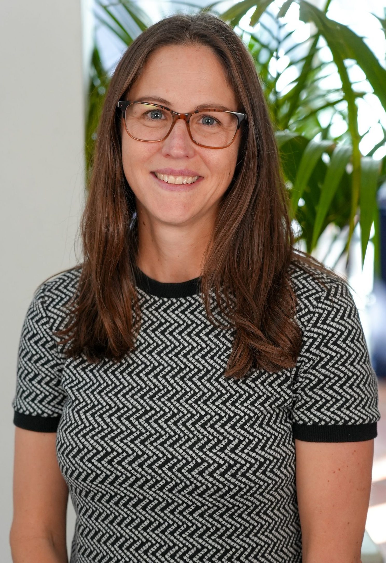 Emily Stenhoff, smiling woman with long brown hair, wearing glasses and a black and white sweater.