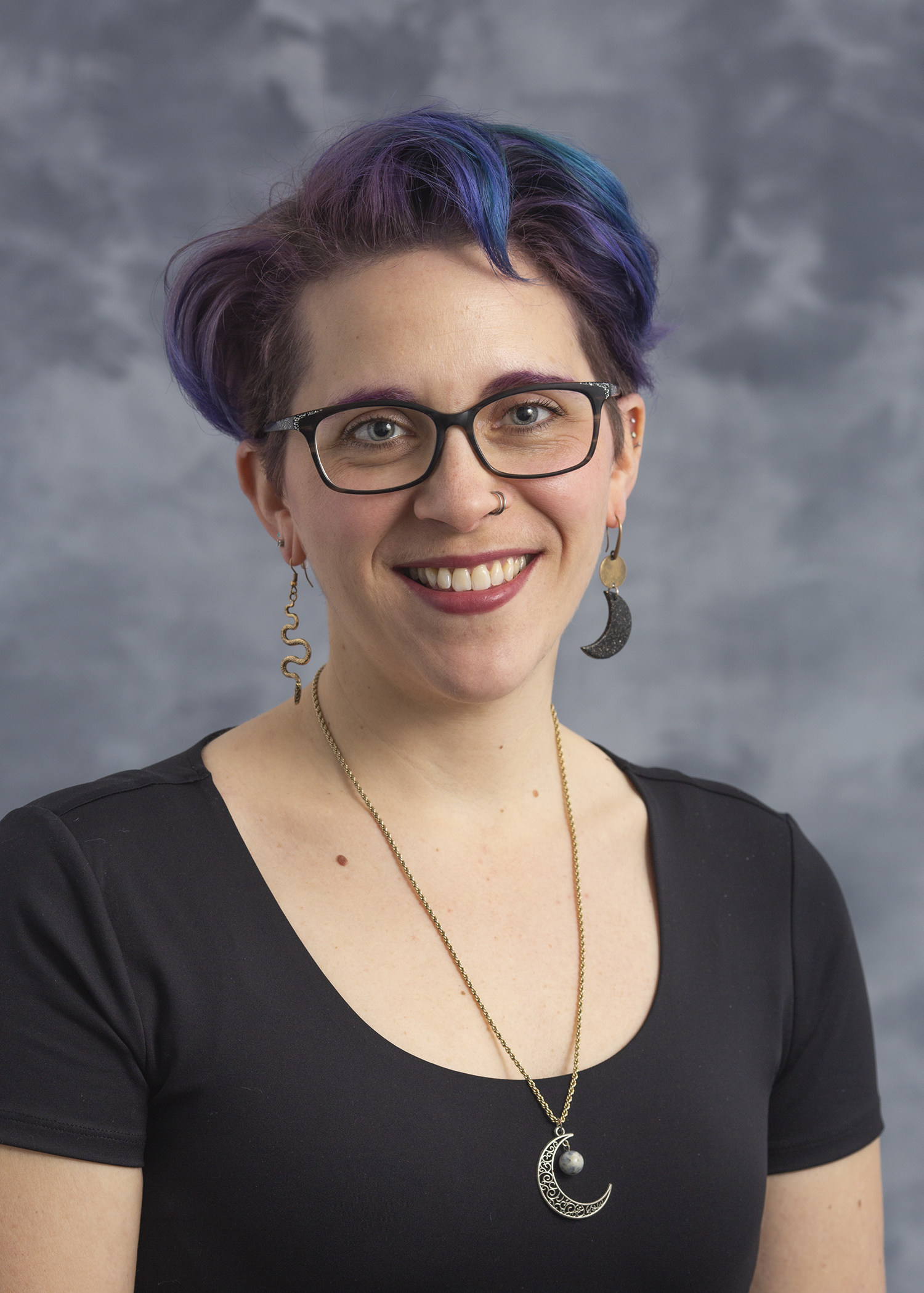 Laura Muller, smiling woman with short, purple hair wearing black glasses and a black shirt.