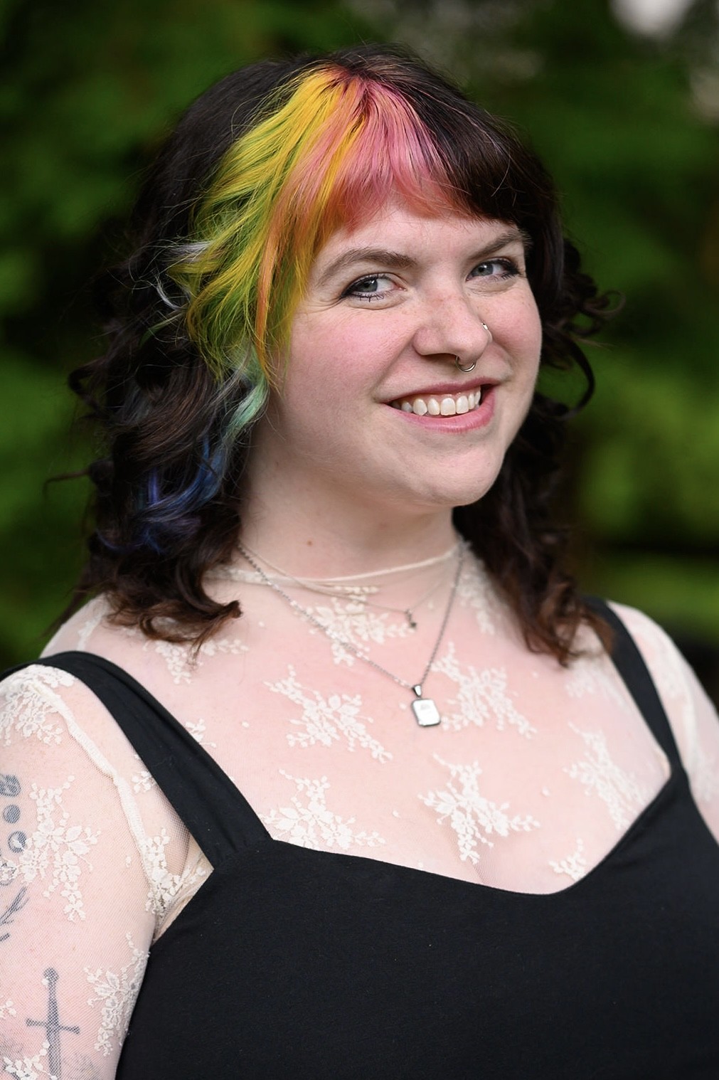 Emily Myers, smiling woman with colorfully highlighted hair wearing a black shirt with straps over a lace layering top.