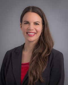 Claire Dalle Molle, smiling woman with long, dark hair wearing a black blazer over a red blouse.