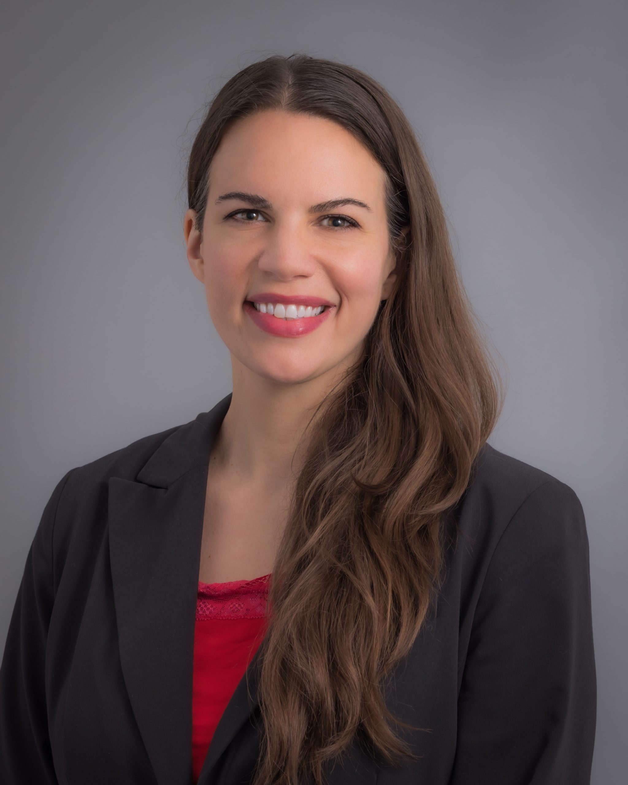Claire Dalle Molle, smiling woman with long, dark hair wearing a black blazer over a red blouse.